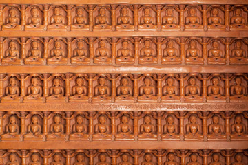 Background of carved wall with many Buddha figures sitting in yoga position.