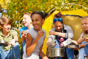 African girl cooks soup in pot for friends
