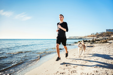 Running man. Male runner jogging with siberian husky dogs during the sunrise on beach