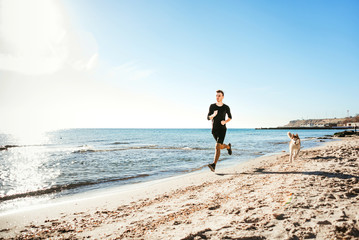 Running man. Male runner jogging with siberian husky dogs during the sunrise on beach