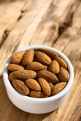 Shelled almonds with seedcoat in small bowl, photographed on wood with natural light (Selective Focus, Focus on the almonds in the middle)