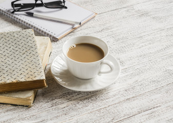 Books, open a blank notepad and a cup of tea with milk on white wooden table