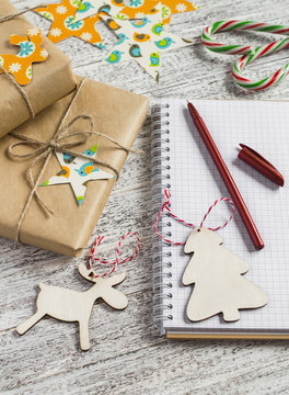 Christmas gifts, Christmas ornaments, candy and an open blank notebook on a light wooden table
