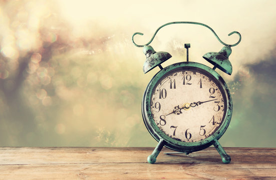 image of vintage alarm clock on wooden table in front of abstract blurred background. retro filtered
