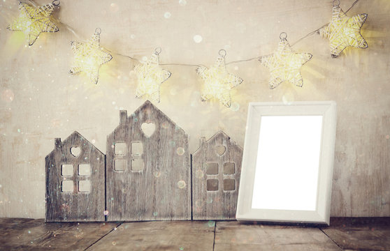 low key image of vintage wooden house decor, blank frame on wooden table and stars garland. retro filtered with glitter overlay. selective focus

