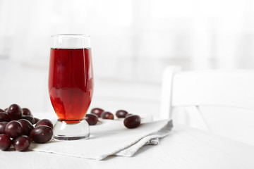 Glass of juice and ripe grapes in bowl on wooden table