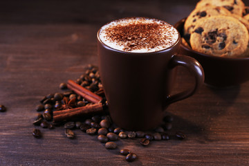 Cup of coffee decorated with roasted beans, cinnamon and cookies around on wooden background
