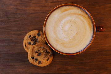 Cup of coffee with milk foam and  cookies with chocolate crumbs on wooden background