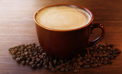 Brown ceramic cup of coffee decorated with roasted beans around on wooden background, close up