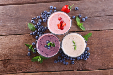 Fototapeta na wymiar Tasty blueberry, strawberry and milk yogurts with berries and mint around on wooden background