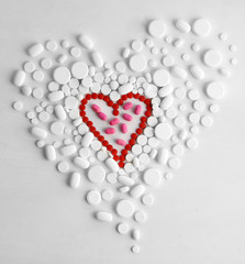 Heart of red pills on white pills background