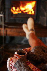 Woman resting with cup of hot drink near fireplace