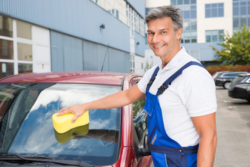 Happy Male Worker Cleaning Car Windshield With Sponge