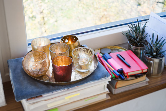 Books, candles, plants and writing instruments on a windowsill. Selective focus on red candle.