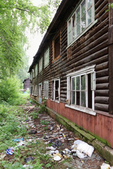 Old wooden two-story abandoned building with garbage in summer