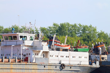 Parts of rusty cargo ships with lifeboats on river at summer 