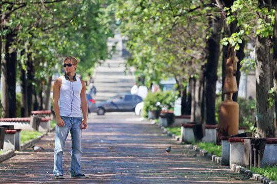 Man in sunglasses stands on alley with green trees and benches 