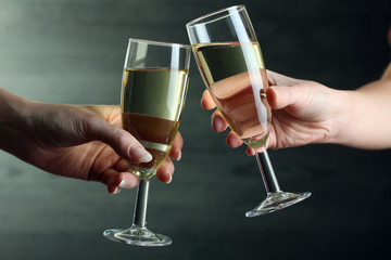 glasses of champagne in hands of the woman on grey background