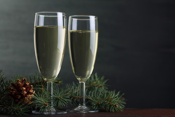 glasses of champagne and a sprig of spruce on a brown wooden table on grey background