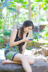 Naklejka premium Biracial teen girl sitting on rock looking at cellphone