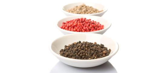 Black, white and pink peppercorn in white bowl over white background