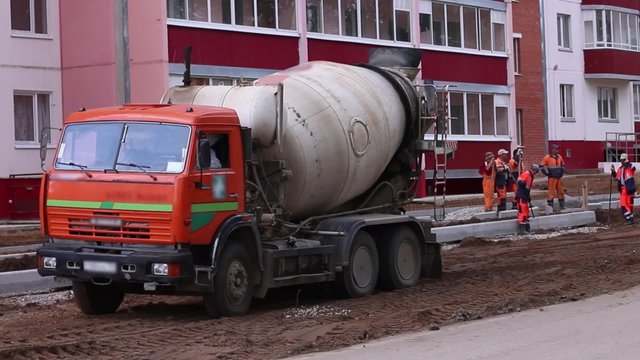 Concrete mixer works on construction and workers stand near it
