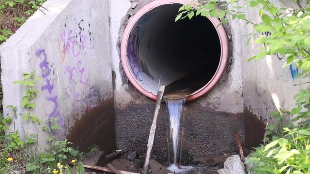 Wastewater pipe with dirty water flowing among debris in city
