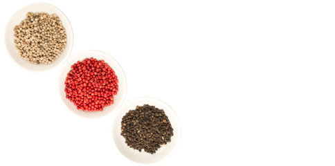 Black, white and pink peppercorn in white bowl over white background