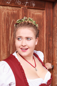 Gesichtportrait einer  jungen bayerischen Frau im Dirndl mit gro&szlig;en Dekolette , geflochtenem Haar und Blumenkranz auf dem Kopf.
