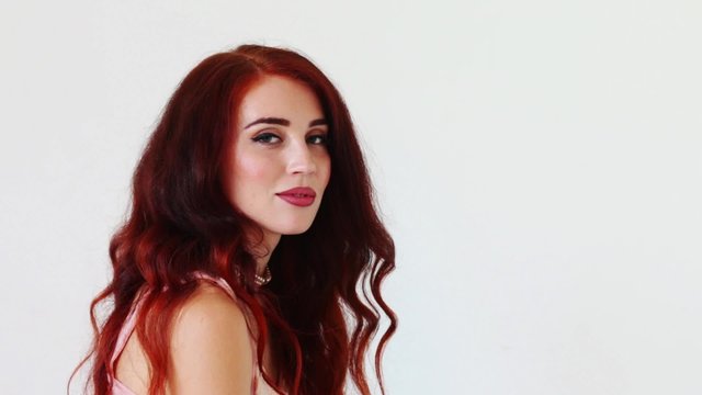 Beautiful young woman with red hair turns her head and looks at camera
