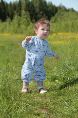 Happy little cute baby stands on green grass near forest