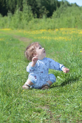 Happy little cute baby sits on green grass near forest