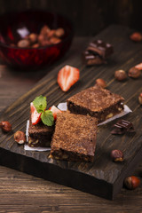Homemade chocolate brownies with hazelnuts on grunge brown wooden background. Toned image. Selective focus