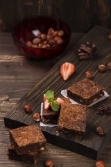 Homemade chocolate brownies with hazelnuts on grunge brown wooden background. Toned image. Selective focus