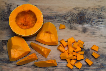 Cut into large and small pieces of pumpkin on a wooden backgroun