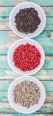 Black, white and pink peppercorn in white bowl over wooden background