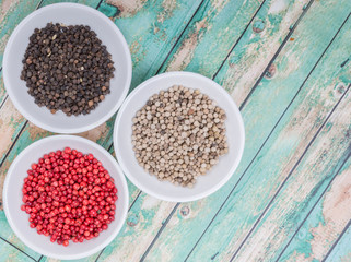 Black, white and pink peppercorn in white bowl over wooden background