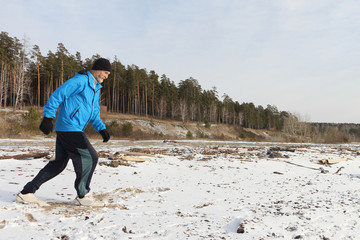 The man in a blue jacket running on snow on the river bank