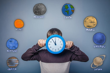 Teen boy covered his face with a clock planet of the solar syste