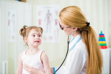 Pediatrician woman examining cute little girl with stethoscope. Kid happily smiling and looking at the doctor