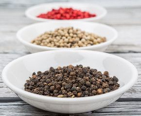 Black, white and pink peppercorn in white bowl over wooden background