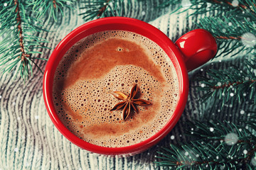 Red cup of hot cocoa or hot chocolate on knitted background with fir tree, traditional beverage for winter time, vintage toned