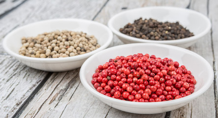 Black, white and pink peppercorn in white bowl over wooden background
