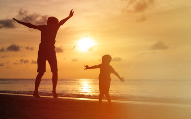 father and son jumping at sunset beach