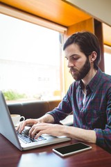 Hipster student using laptop in canteen