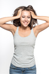 Awesome Caucasian attractive sexy female model with brunette hair is grimacing in studio, wearing grey sleeveless shirt and jeans, isolated on white background