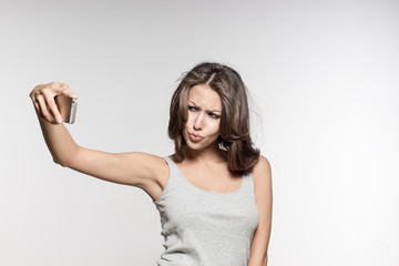 Fototapeta premium attractive female model is grimacing, making selfies, grey shirt and jeans, white background