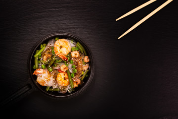 Glass noodle with shrimps and green vegetables in cast-iron pan. Healthy food concept. Top view. Toned image