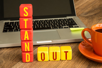 Stand Out written on a wooden cube in front of a laptop