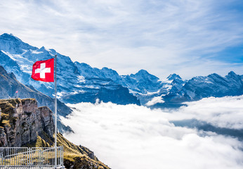 Red Swiss flag at Swiss Alps over mountains and clouds.